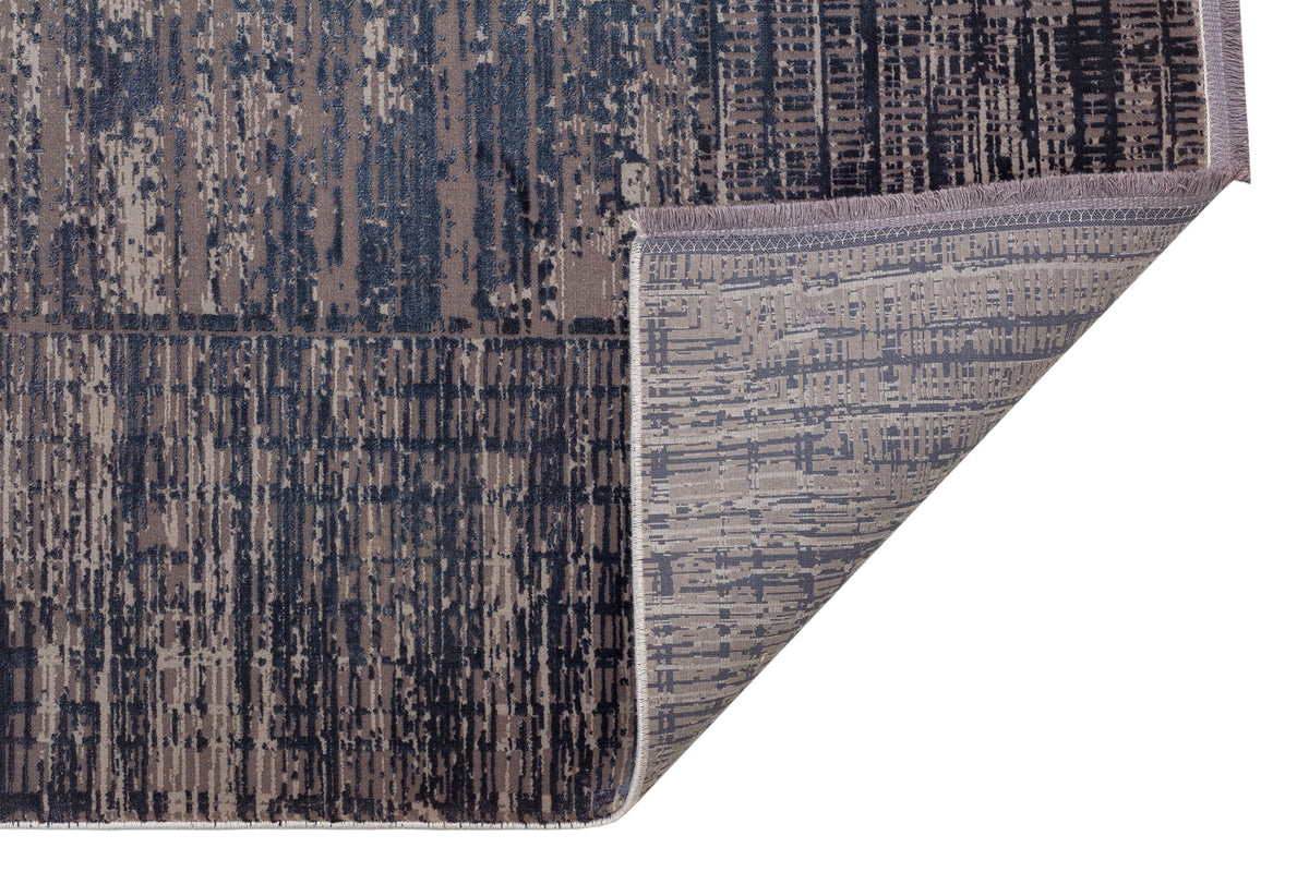 Navy and grey abstract distressed rug with a folded corner showing the woven backing and fringe detail.