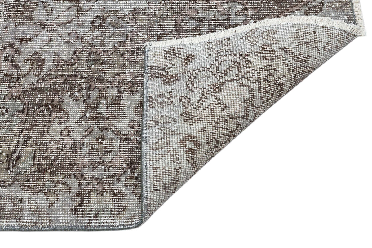 Brown and grey distressed traditional rug with a floral medallion pattern, shown with a folded corner revealing the backing.