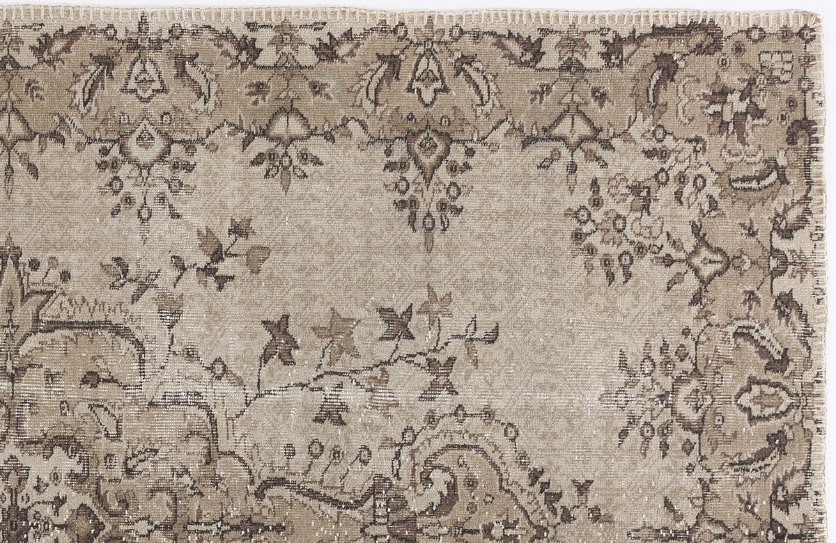 Beige and brown vintage-style rug with a distressed floral medallion pattern and a stitched edge.