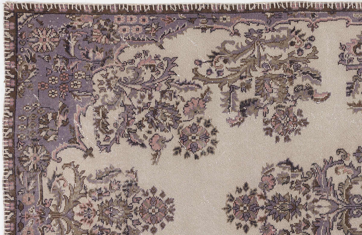 Beige rug with a distressed floral medallion pattern in muted purple, brown, and pink tones.