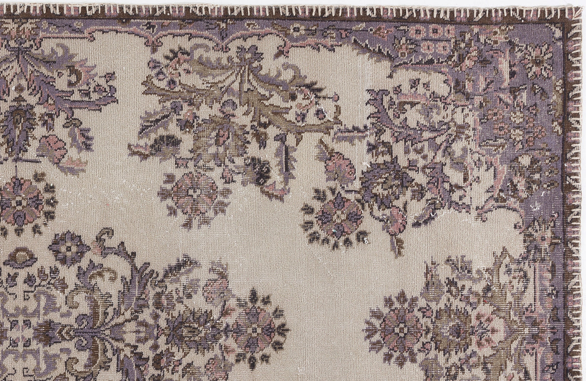 Beige rug with a distressed purple and brown floral medallion pattern and a dark brown stitched border.