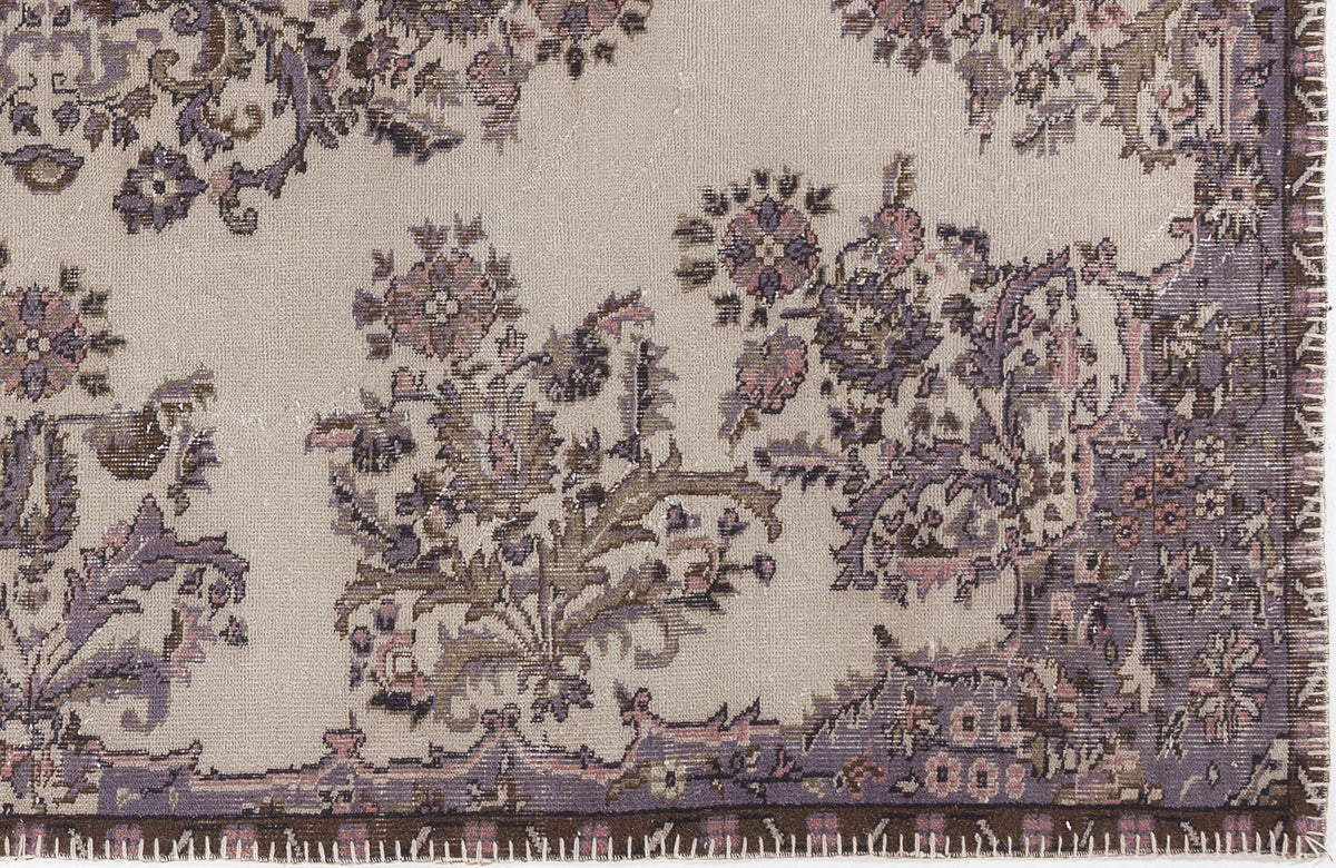 Beige rug with a distressed floral pattern in muted purple, brown, and pink tones, featuring a stitched edge border.
