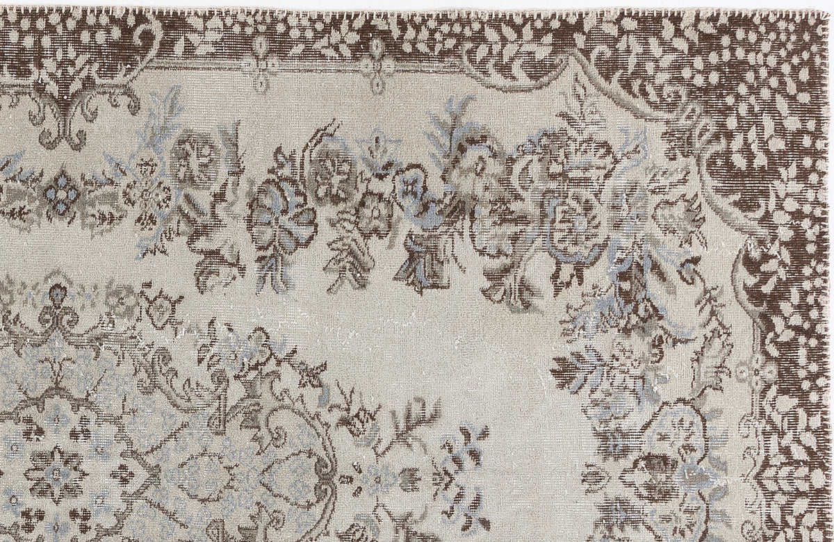 Beige rug with a distressed brown and light blue floral medallion pattern and a decorative border.