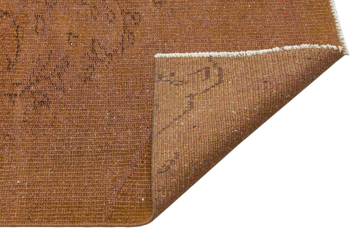 Tobacco brown rug with a faint, distressed floral pattern and a folded corner showing the woven texture.