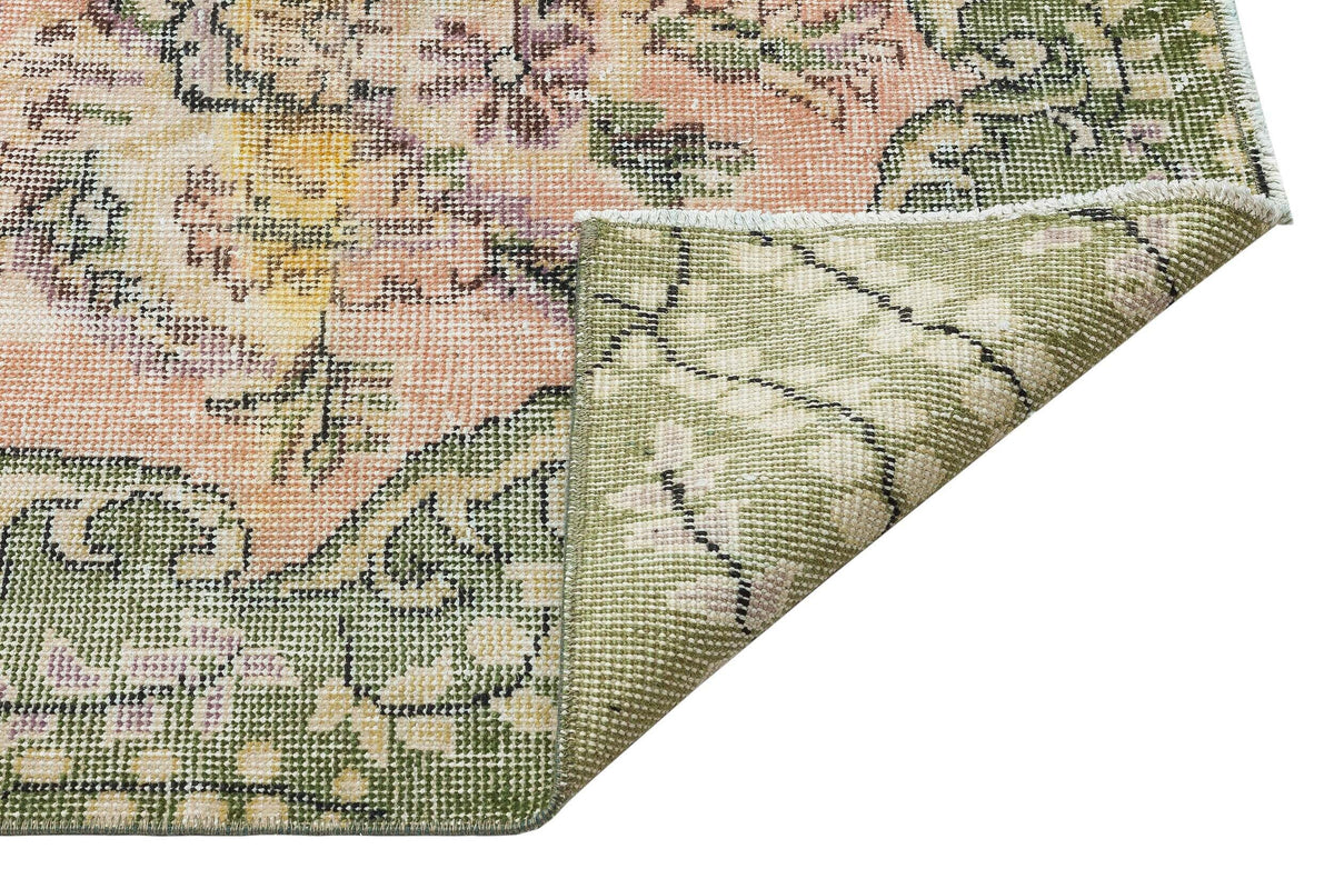 Distressed floral rug in sage green, peach, and yellow with a folded corner revealing the woven backing.