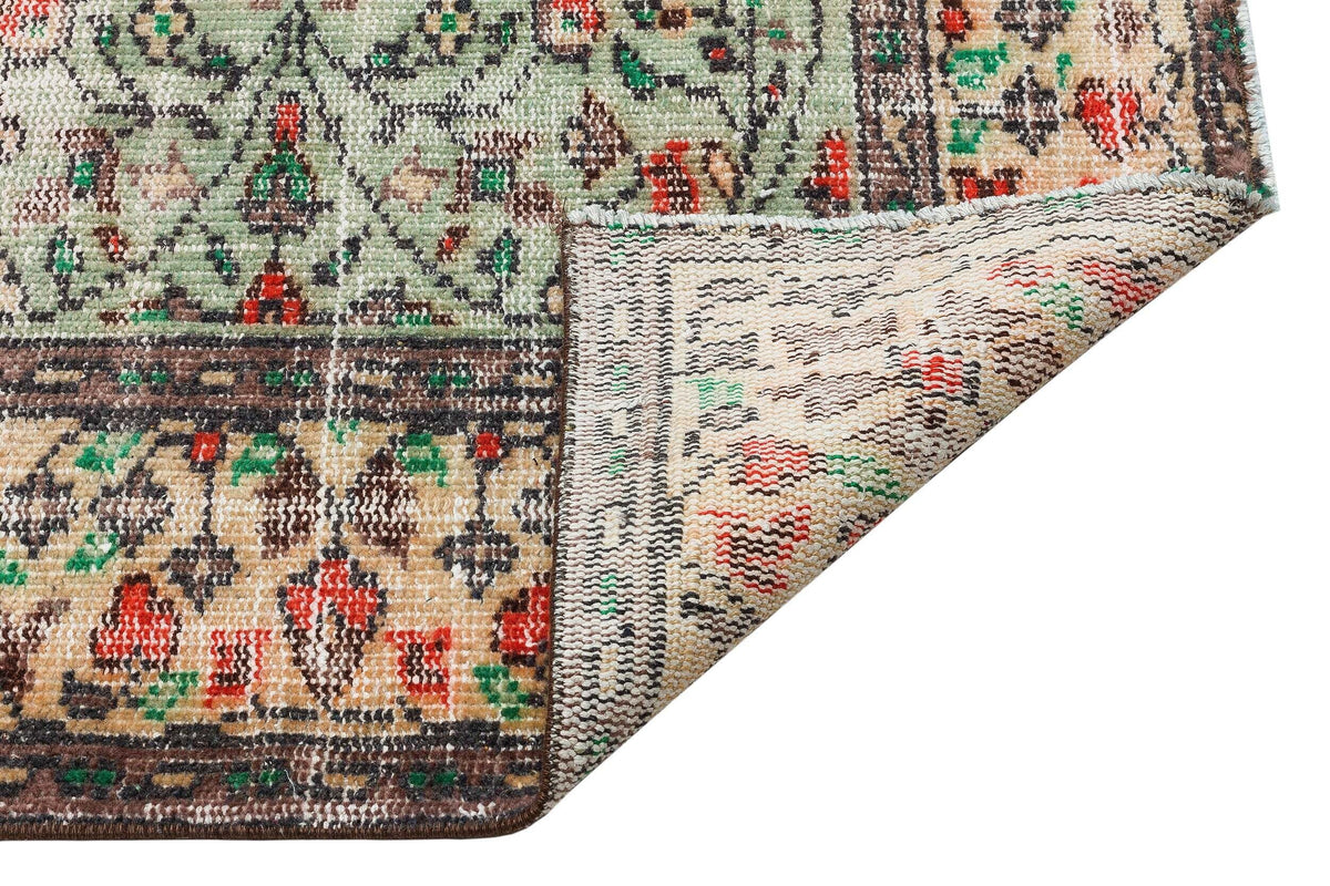 Sage green, beige, and red traditional floral rug with a folded corner revealing the woven backing.
