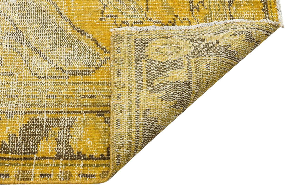 Mustard yellow and brown distressed traditional rug with a folded corner showing the woven backing.