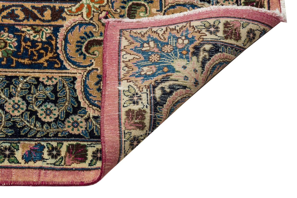 Traditional Persian-style rug with intricate floral patterns in blue, pink, and gold, shown with a folded corner.