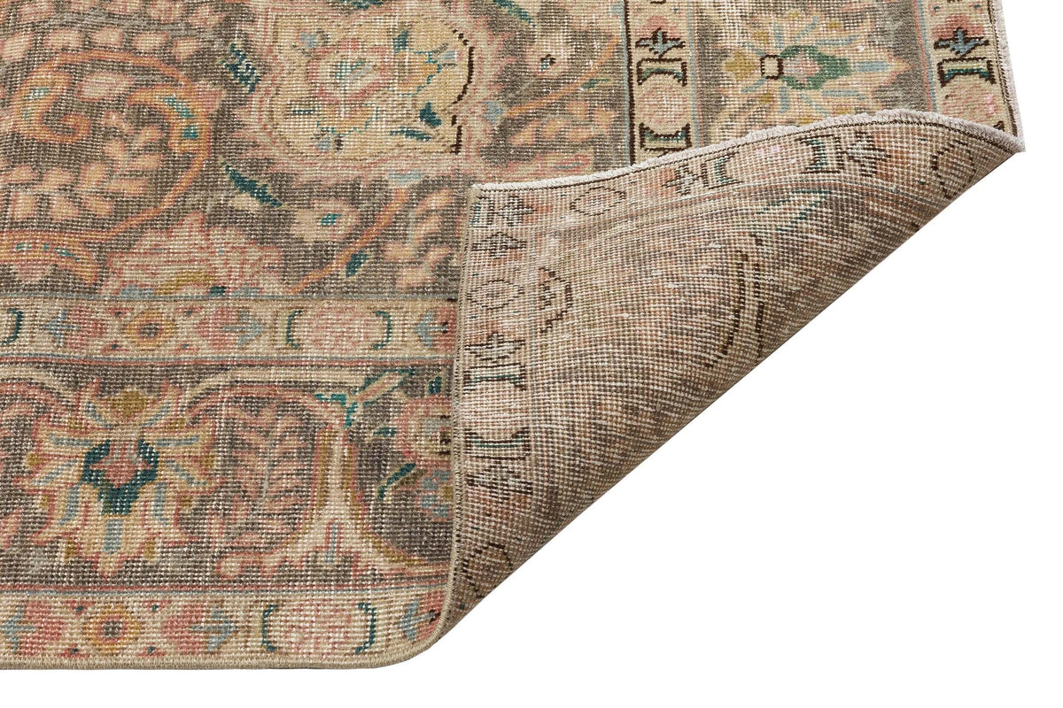 Distressed beige, pink, and teal traditional medallion rug with a corner folded to show the woven backing.