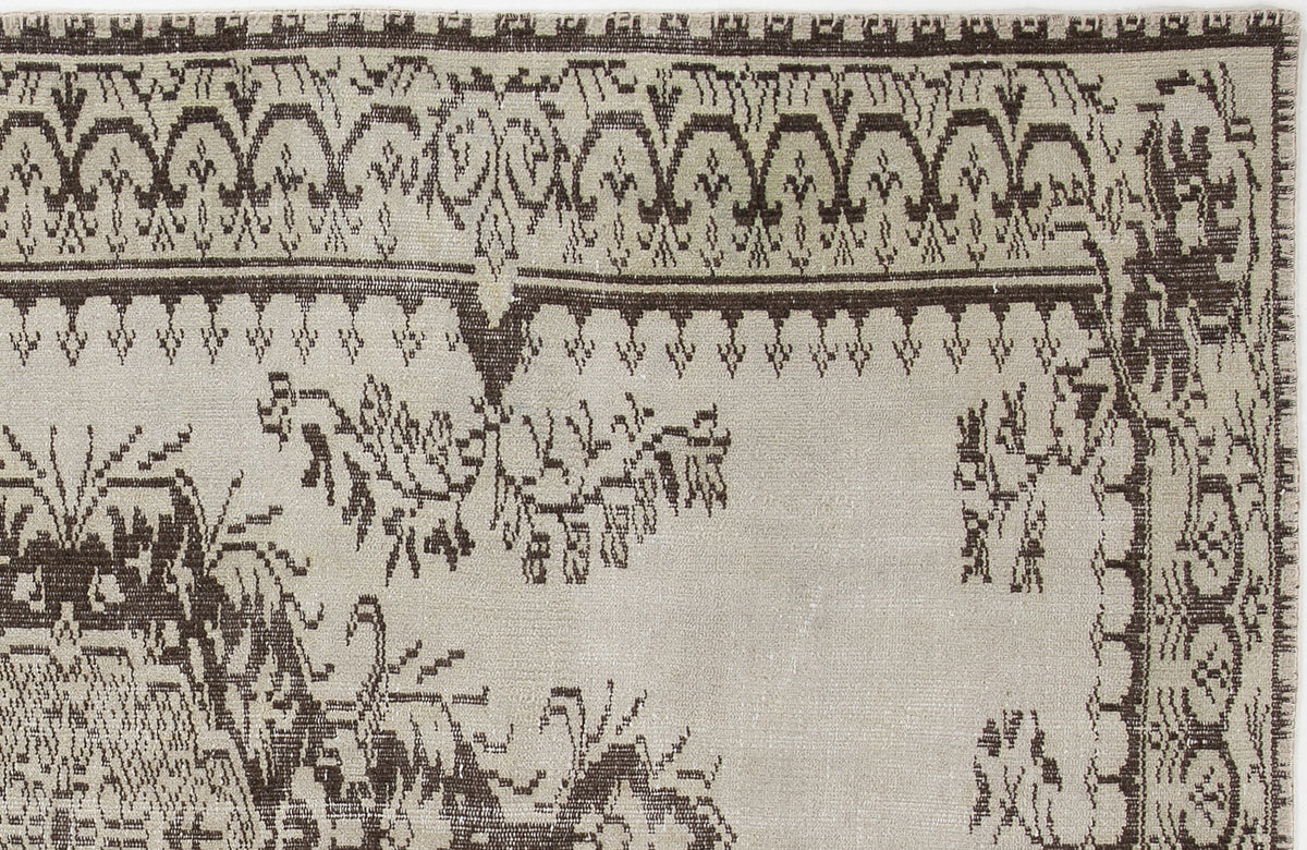Beige and dark brown rug with a traditional geometric border and stylized floral motifs.