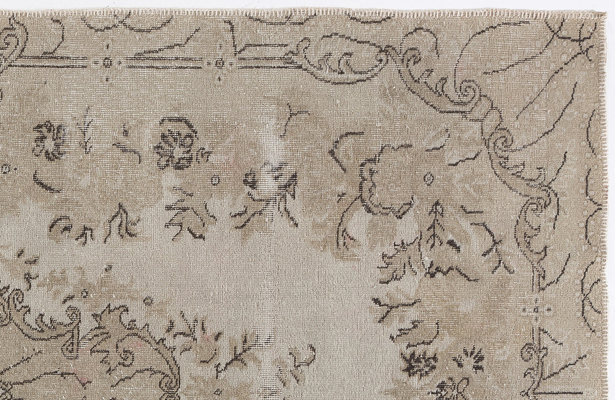 Beige vintage-style rug with a distressed, dark brown floral and scrollwork pattern on a white background.