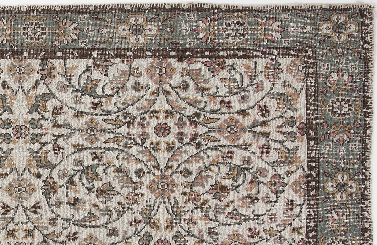 Distressed traditional rug with a cream field, sage green border, and intricate floral vine pattern in muted earth tones.