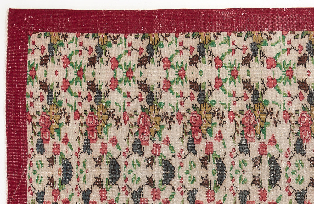 Beige rug with a red border and a repeating floral pattern in red, green, and dark grey.