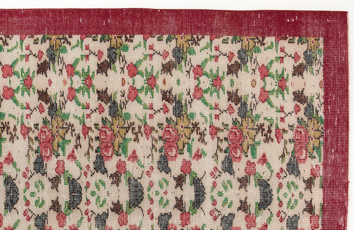 Beige rug with a red border and a repeating floral pattern in red, green, and charcoal.