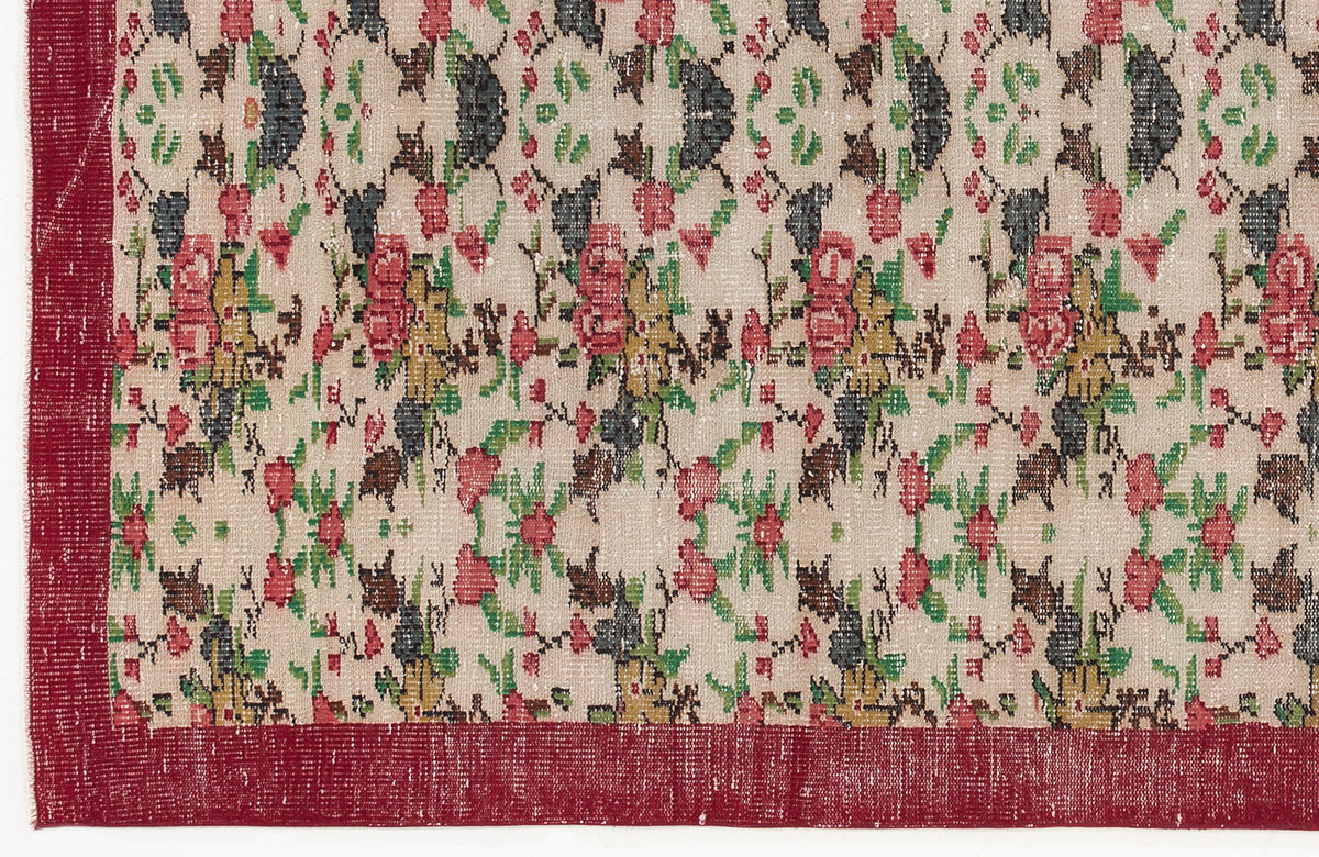 Beige rug with a red border and a repeating floral pattern in red, green, and charcoal on a white background.