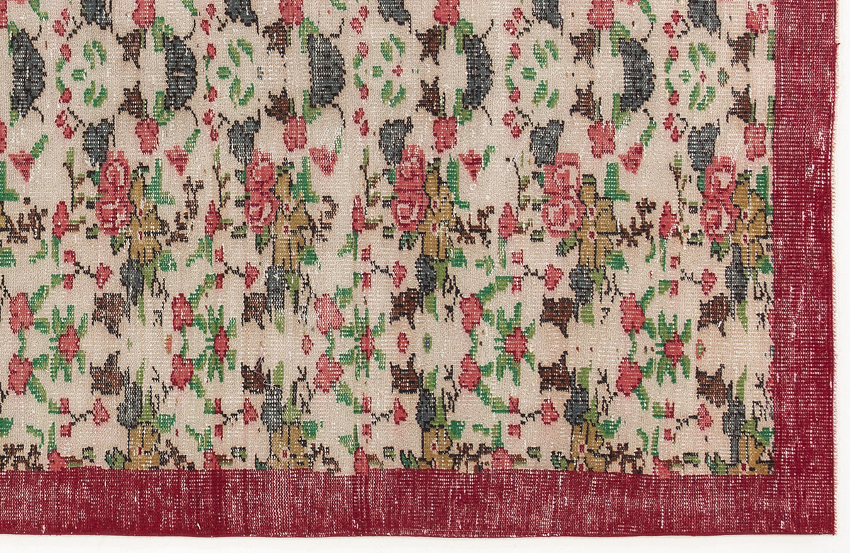 Beige rug with a distressed floral pattern in red, green, and charcoal, featuring a solid red border.