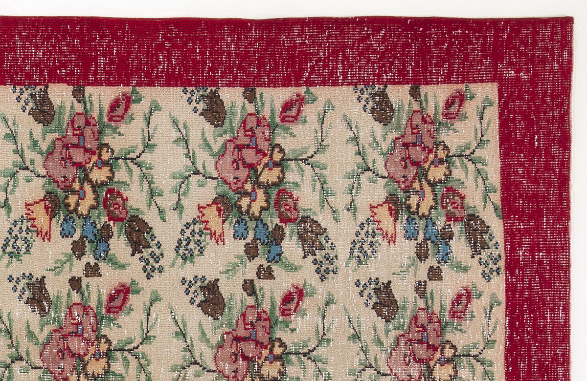 Beige rug with a repeating floral pattern in red, green, and blue, featuring a wide, distressed red border.