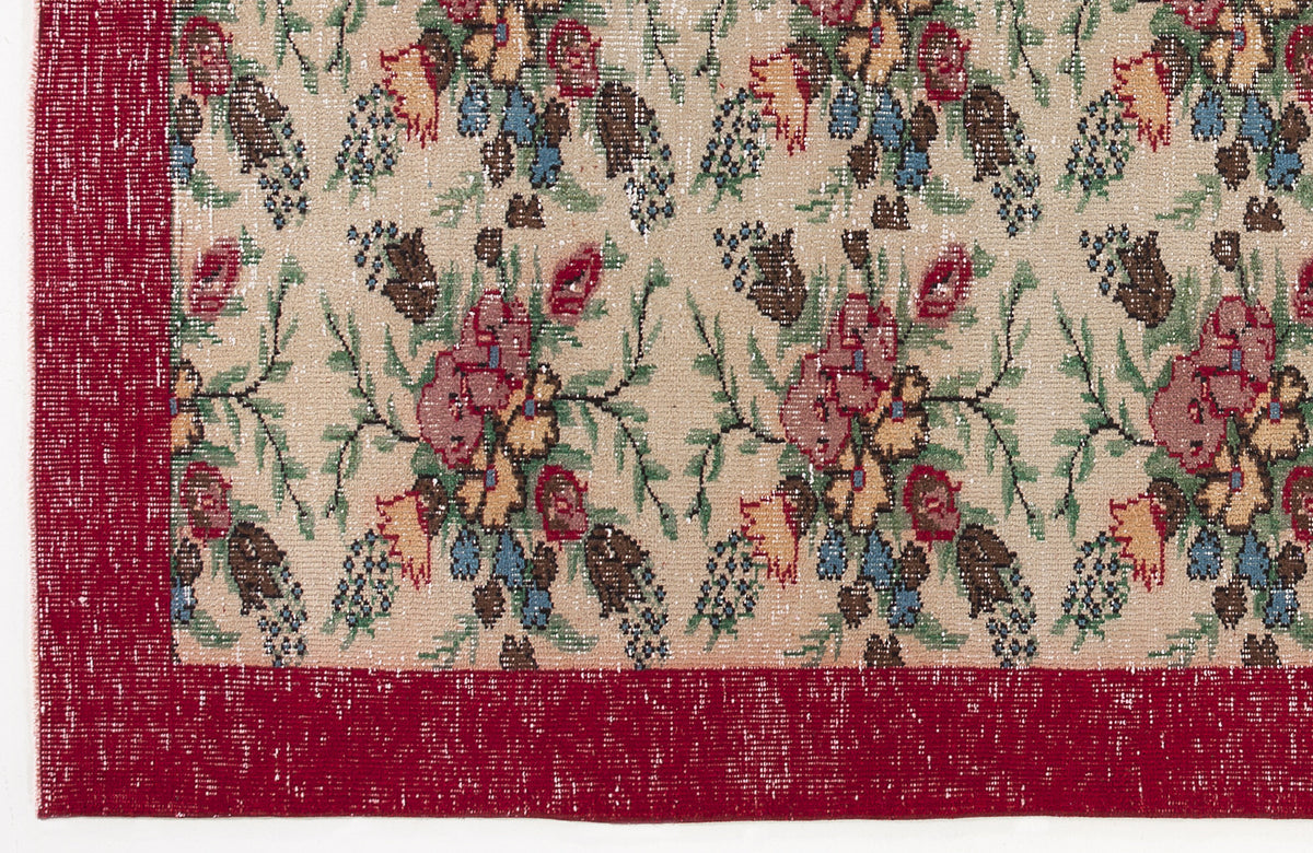 Beige rug with a repeating floral pattern in red, green, and blue, featuring a solid red border.