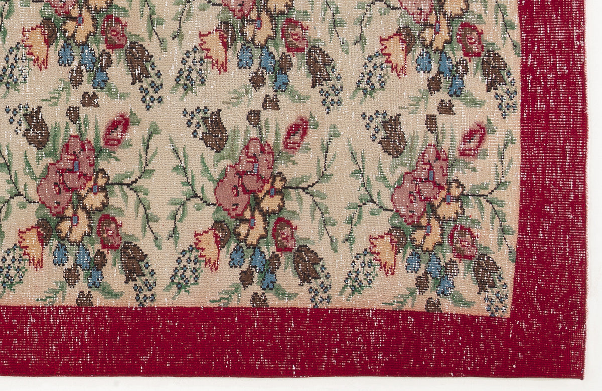Beige rug with a repeating floral pattern in red, blue, and brown, featuring a wide, solid red border.