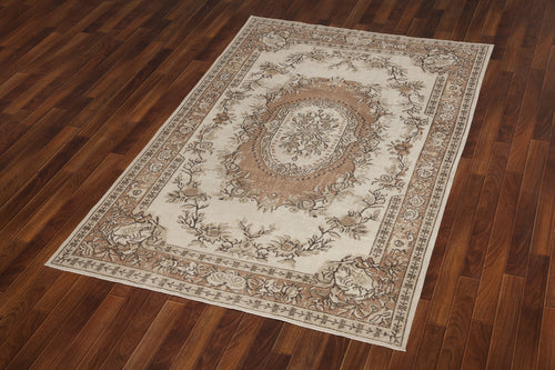 Load image 1 in gallery view. Beige and brown traditional rug with a central floral medallion and ornate border, displayed on a dark wood floor.