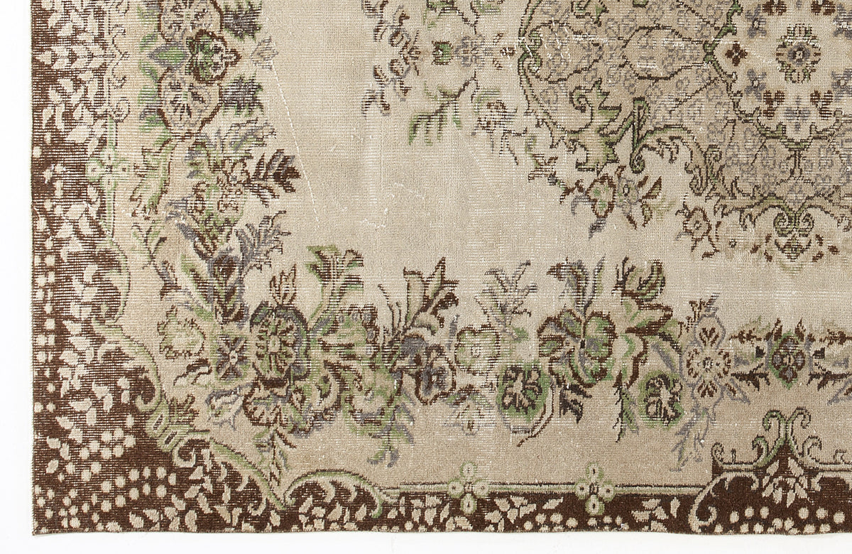 Beige rug with a distressed floral medallion pattern in brown, sage green, and grey.