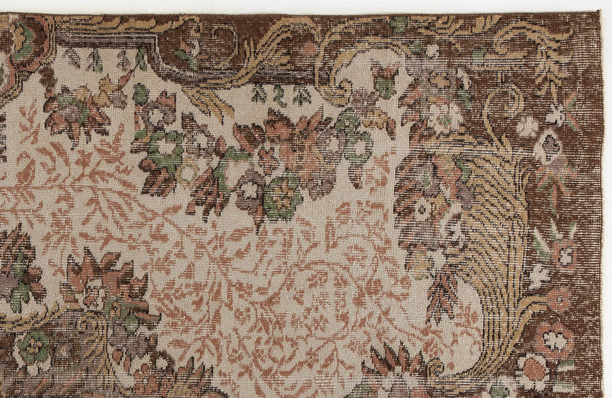 Distressed beige rug with a brown border and intricate floral and vine patterns in muted green, rust, and brown tones.