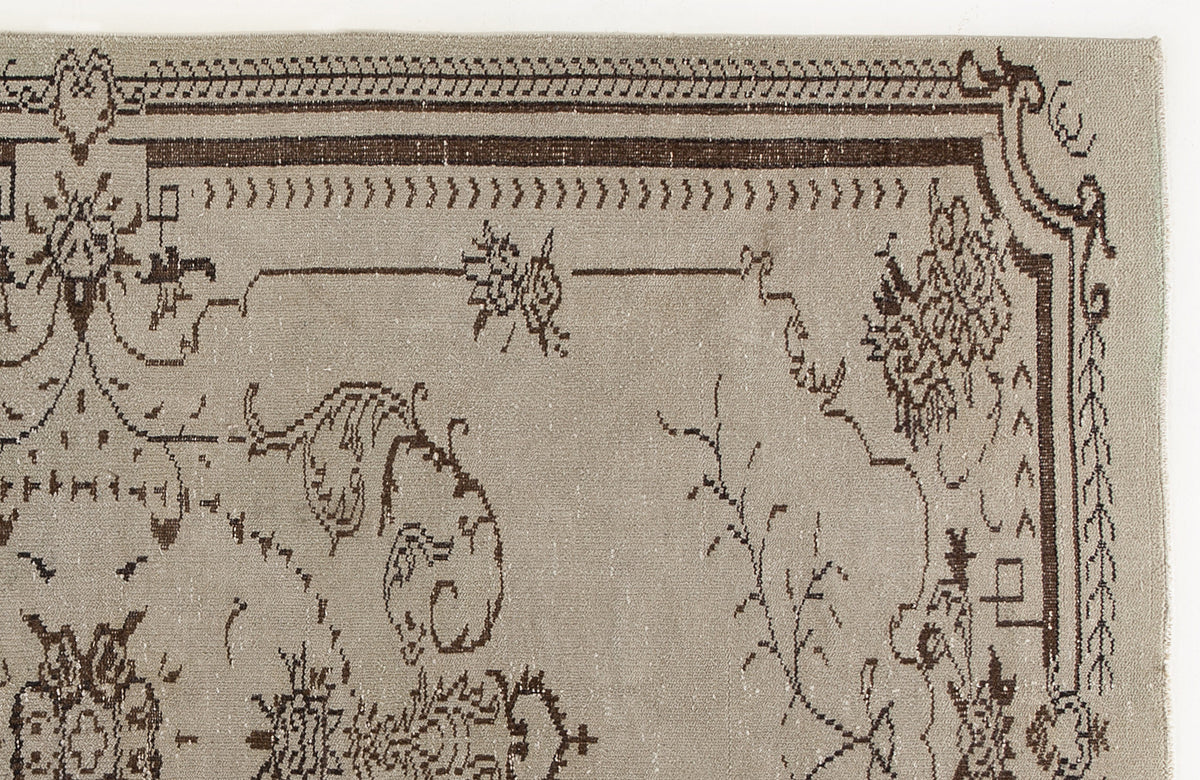 Taupe rug with a dark brown traditional floral border and sparse, stylized botanical motifs.