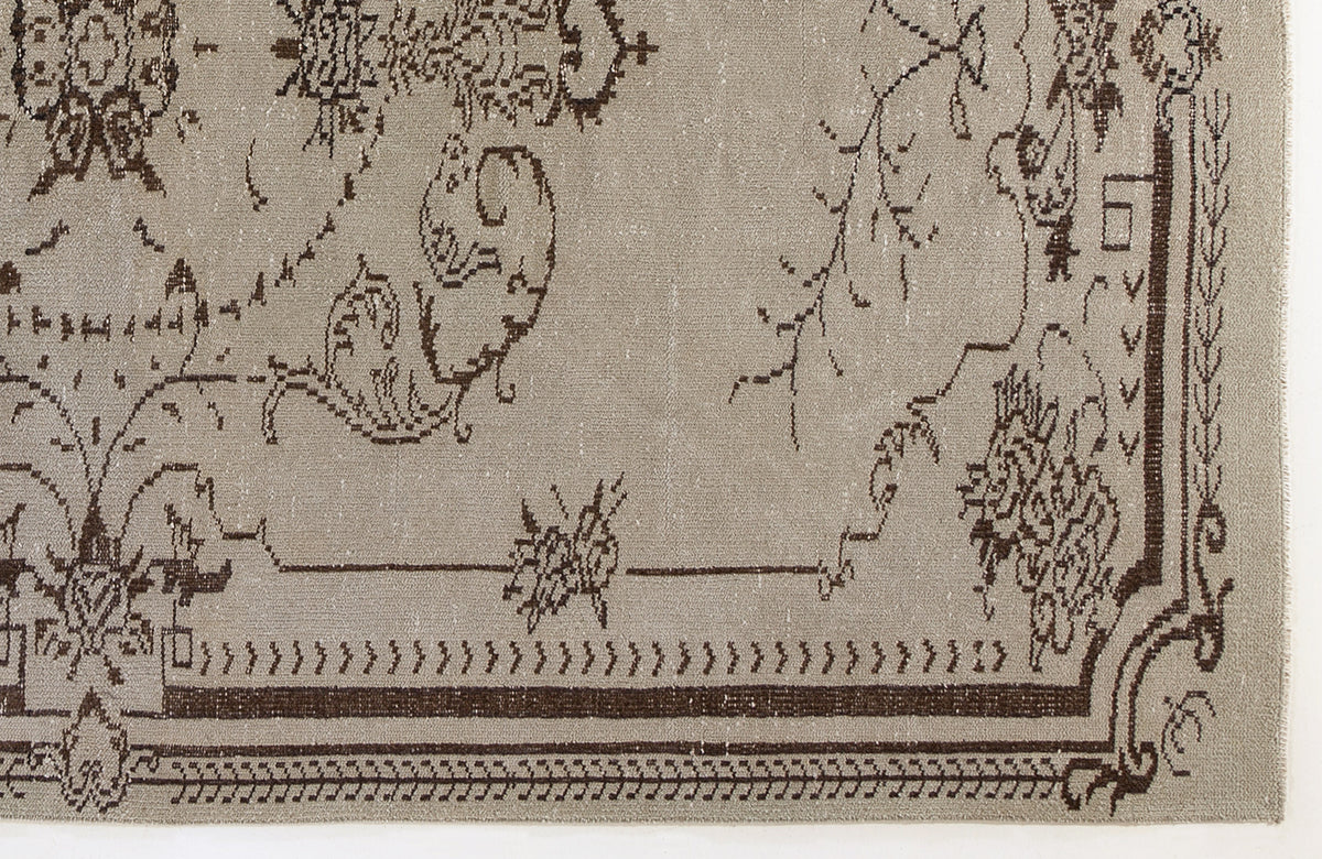 Taupe rug with a dark brown distressed floral medallion pattern and a geometric border.