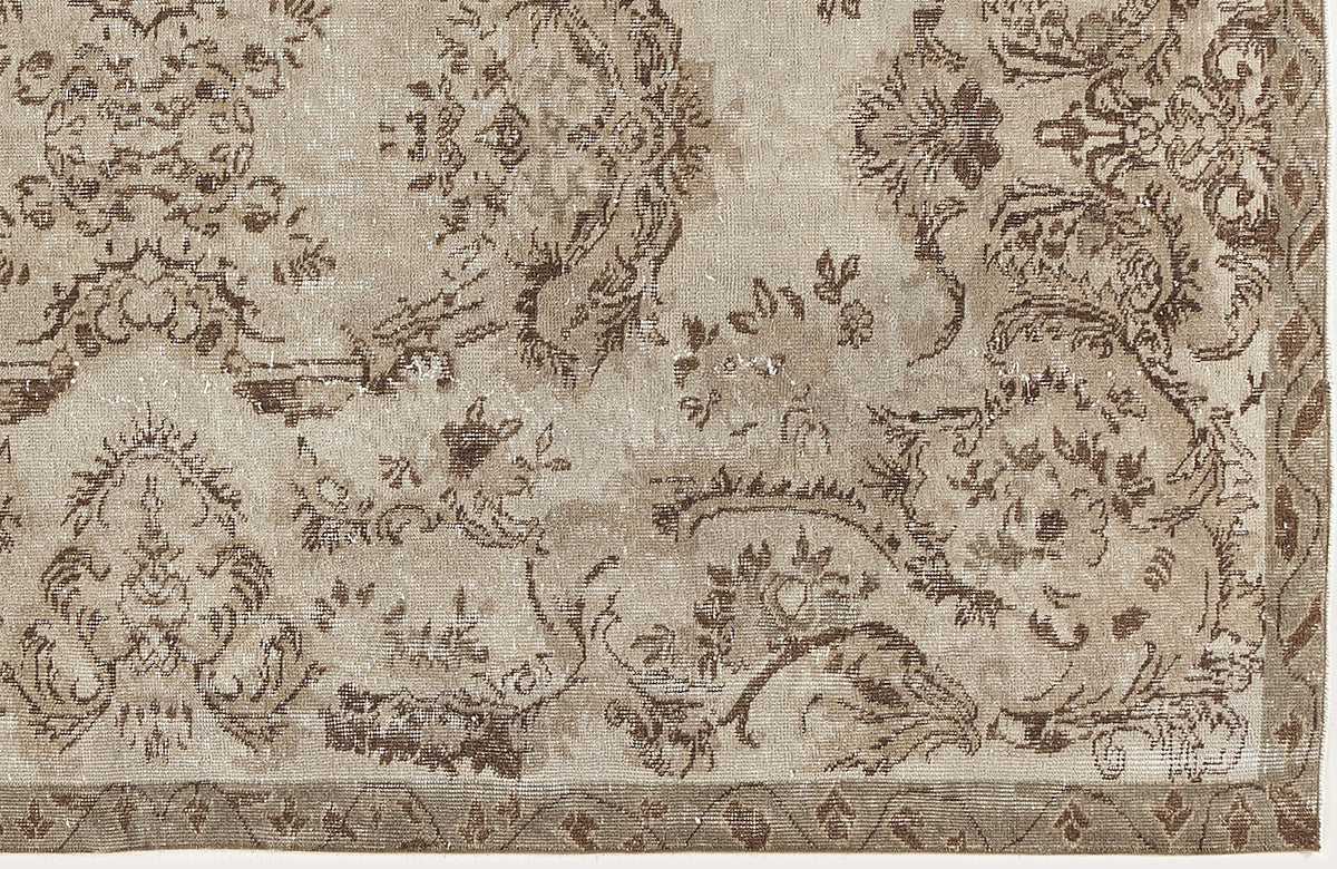 Taupe and brown distressed rug with a traditional floral medallion pattern and a geometric border.