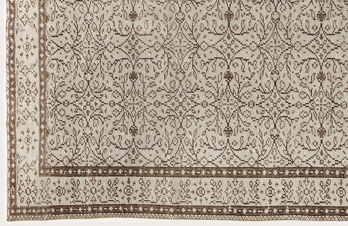 Beige and brown rug with a repeating floral medallion pattern and a decorative geometric border.