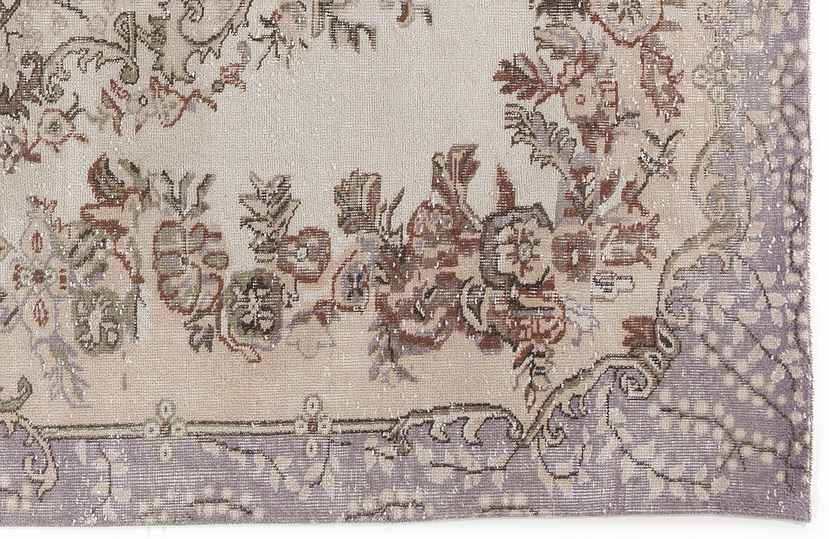 Distressed beige rug with a faded floral medallion pattern in muted brown, sage green, and lavender tones.