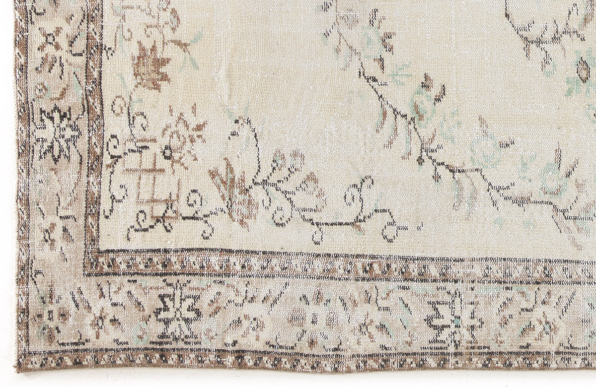 Cream rug with a distressed floral border and central vine pattern in muted brown, grey, and sage green.