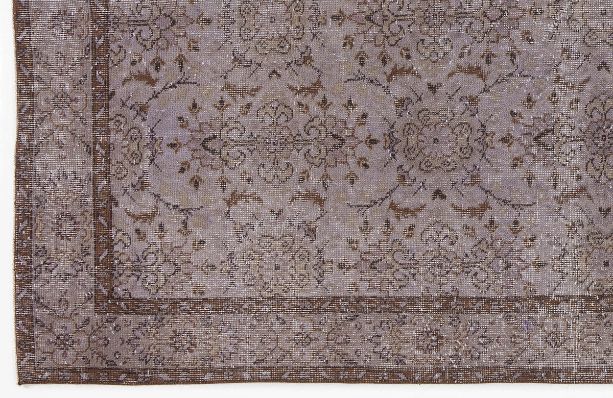 Lavender and brown distressed rug with a traditional floral medallion pattern and a decorative border.