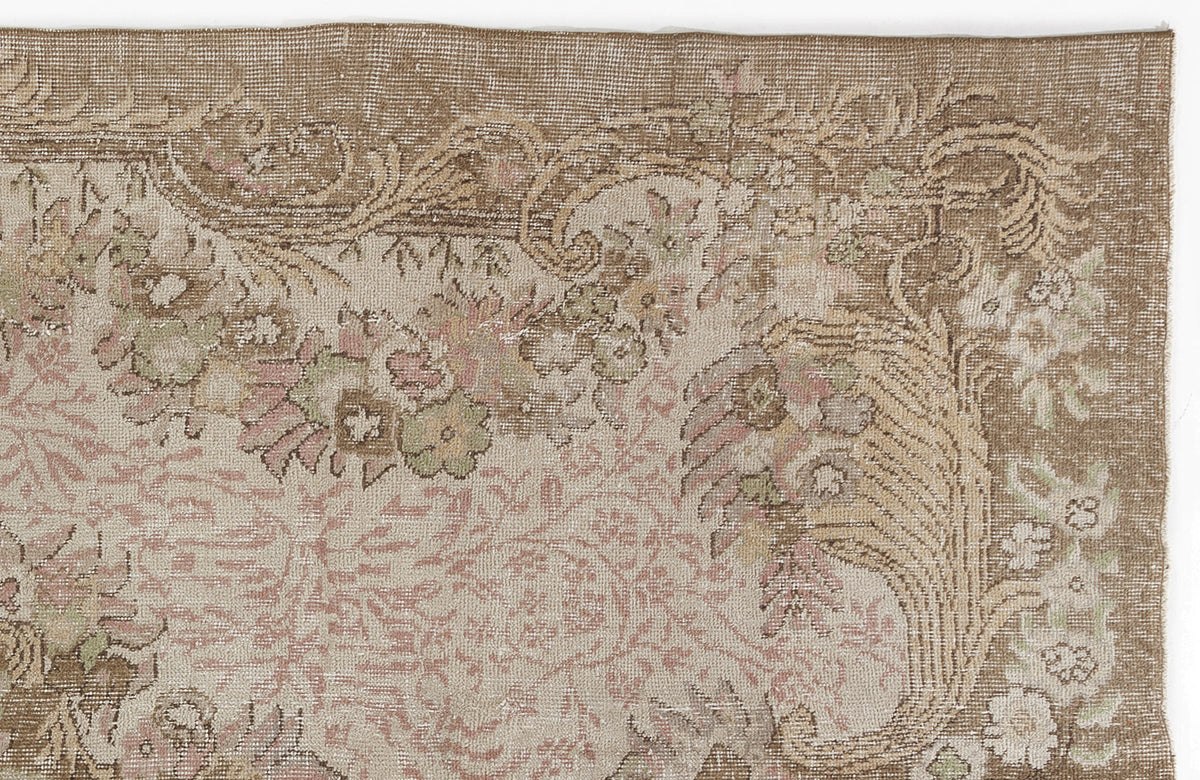 Distressed beige and brown rug with a faded floral medallion pattern and muted pink and sage green accents.