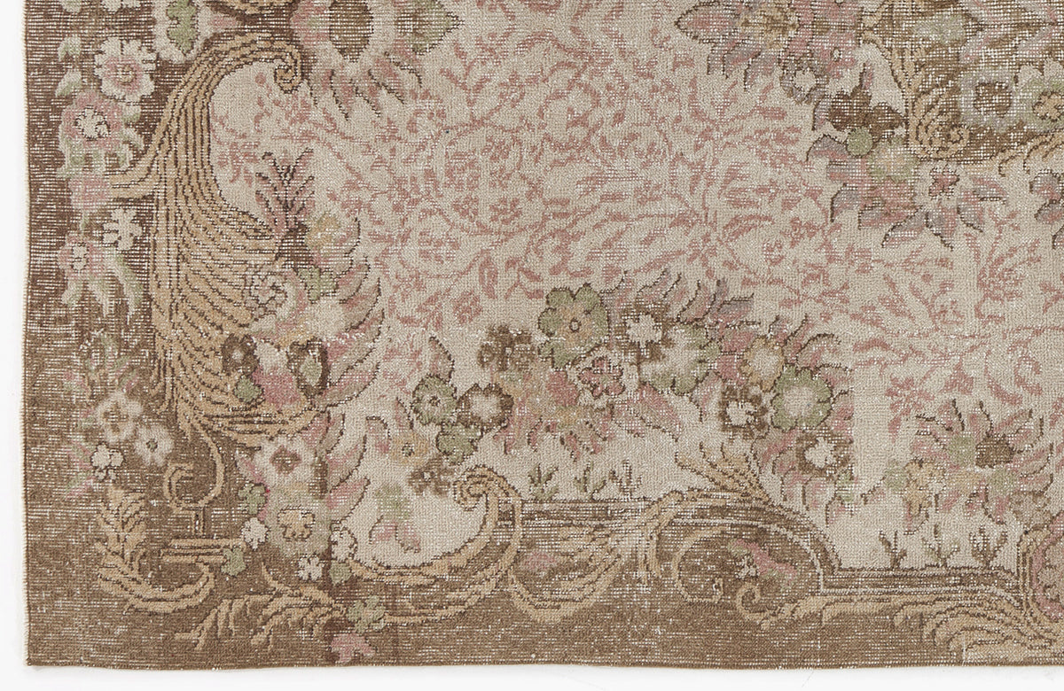 Distressed beige, brown, and muted pink rug with a traditional floral medallion and scrollwork pattern.