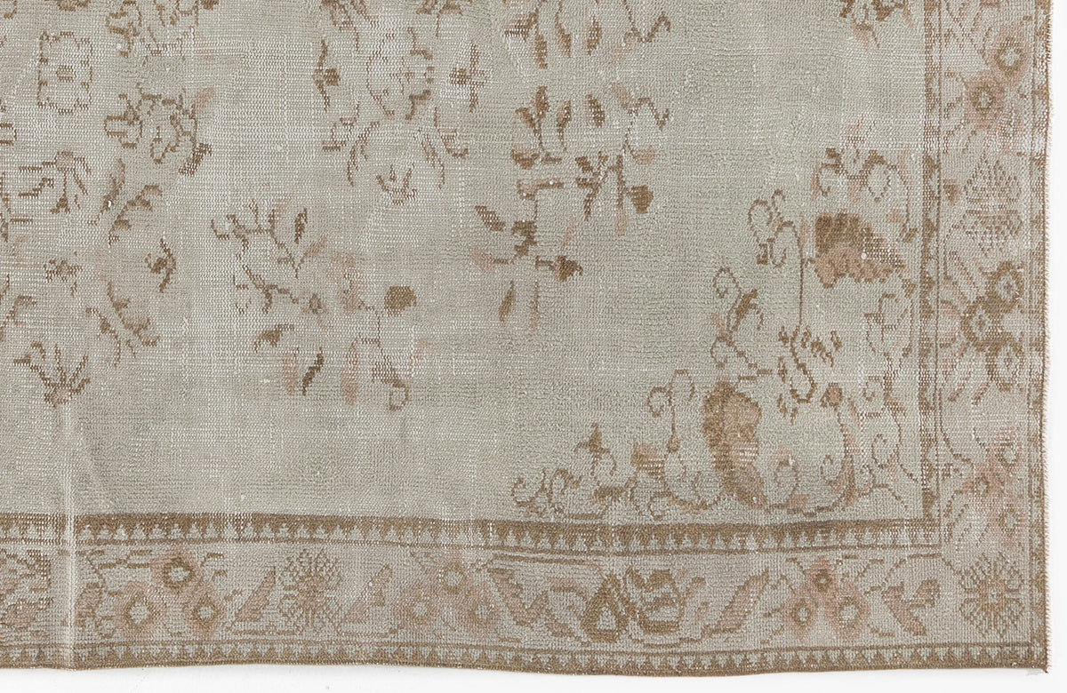 Light gray and beige distressed rug with a faded floral pattern and a detailed geometric border.