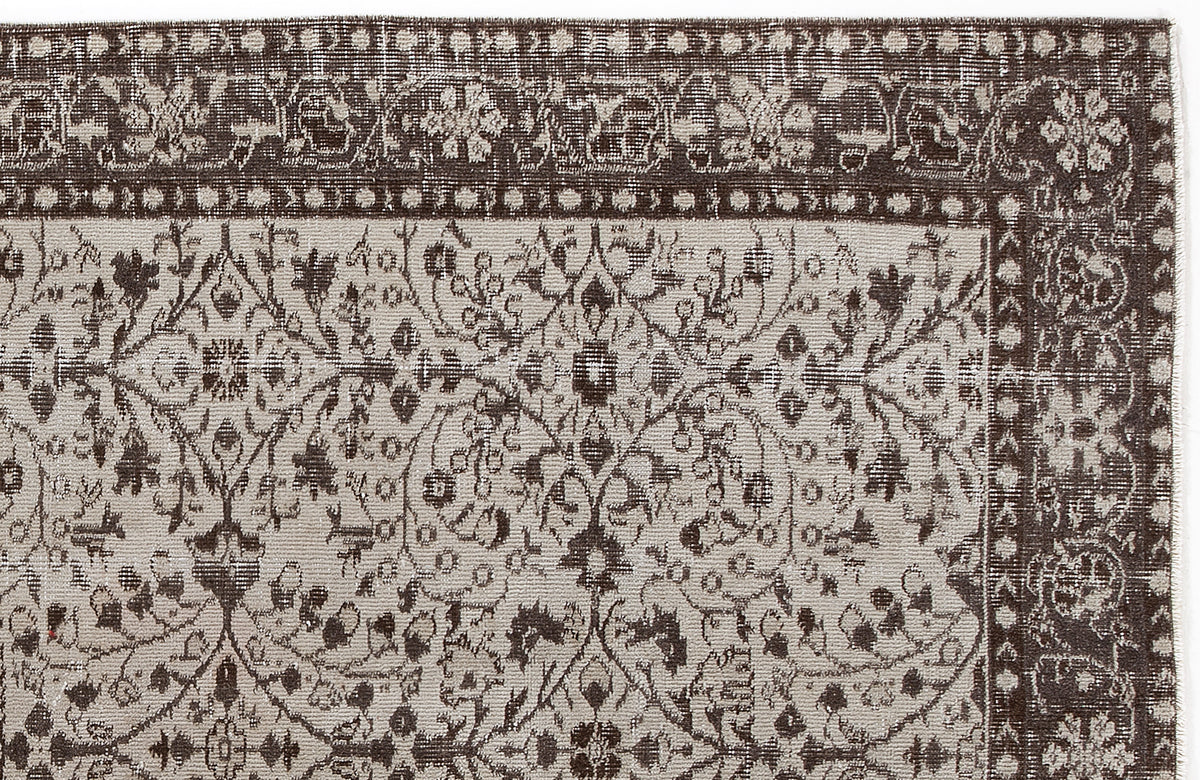 Dark brown and beige vintage-style rug with a distressed floral vine pattern and a decorative geometric border.