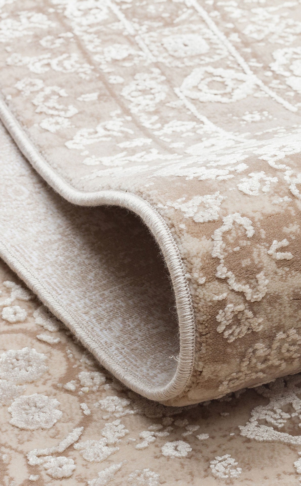 Beige and cream area rug with a distressed floral medallion pattern, shown folded to reveal the serged edge.