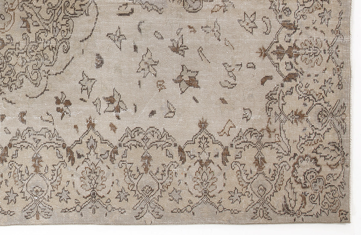Beige and brown distressed rug with a traditional floral medallion border and scattered star-like motifs.