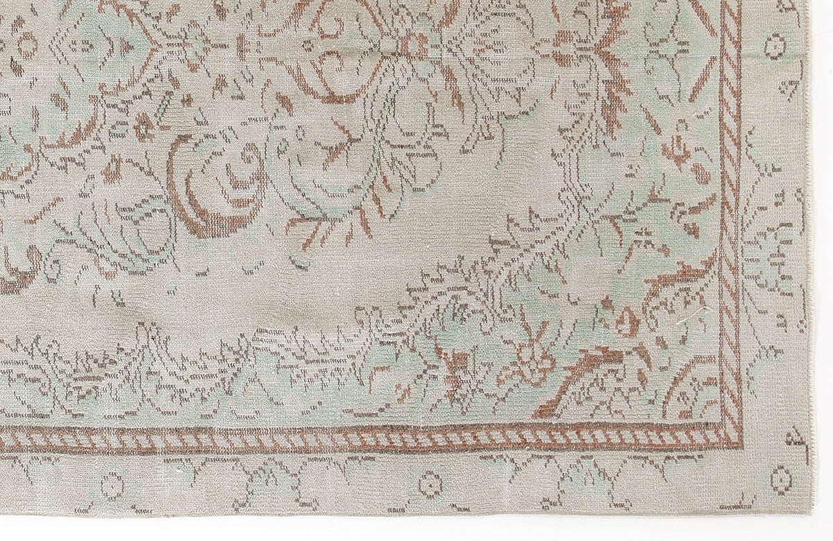 Beige rug with a distressed floral medallion pattern in sage green and terracotta, featuring a braided border.