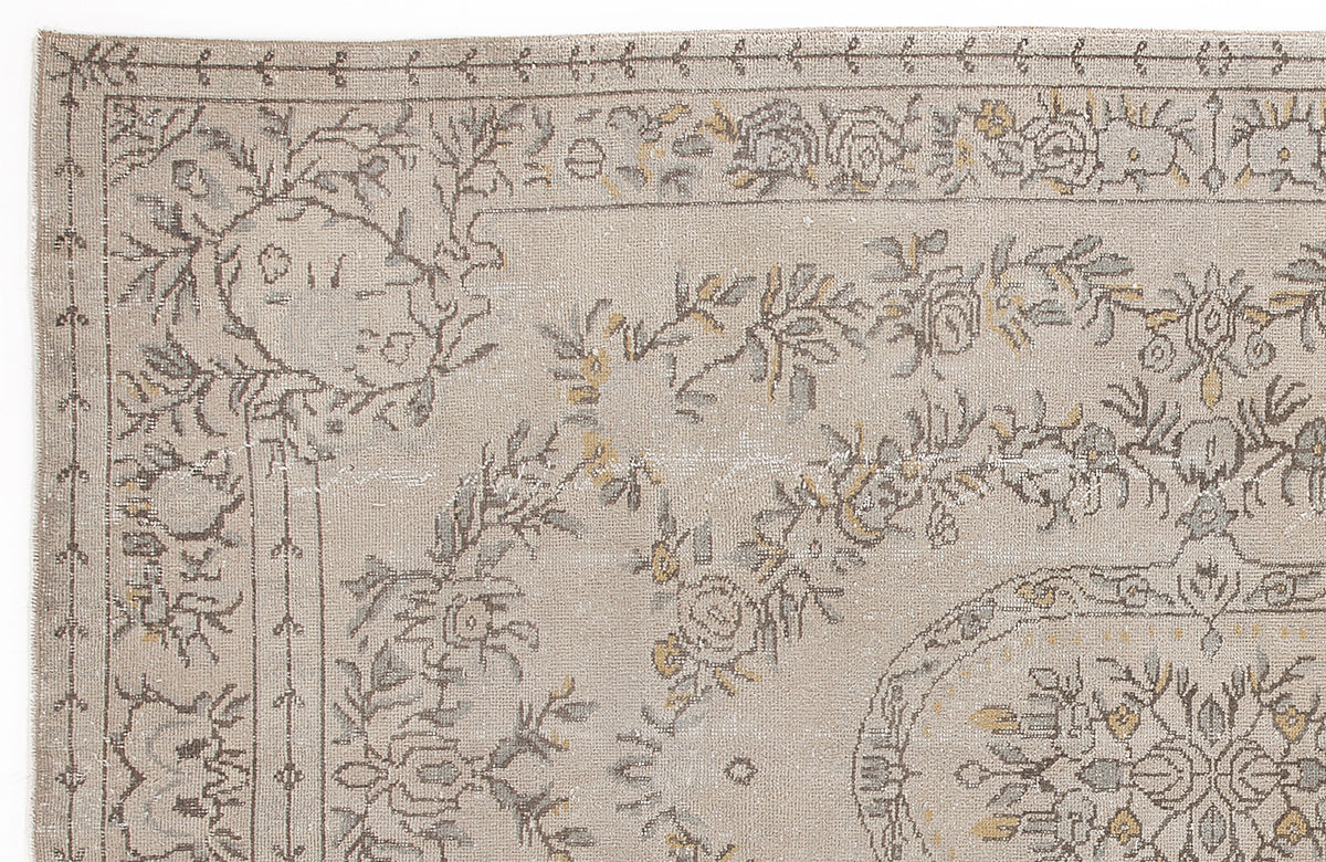 Beige rug with a distressed floral medallion pattern in grey and muted yellow, featuring a decorative border.