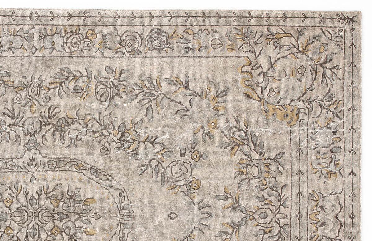 Beige rug with a distressed floral medallion pattern in muted grey and mustard yellow, isolated on a white background.
