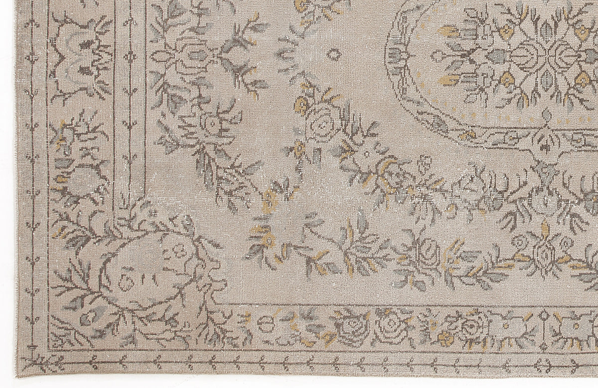 Beige rug with a distressed floral medallion pattern in grey and muted yellow, featuring a decorative border.