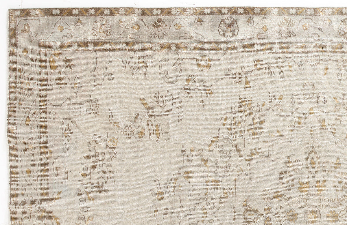 Beige and tan rug with a faded floral pattern and a geometric border on a white background.