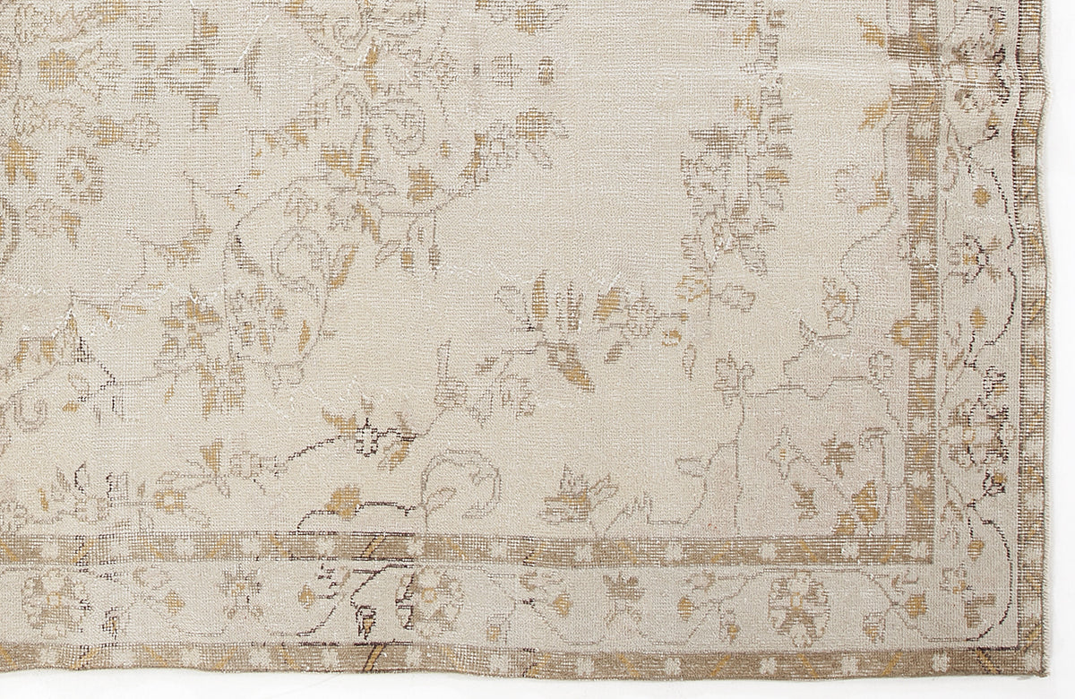 Beige and tan rug with a faded, distressed floral pattern and a decorative geometric border.