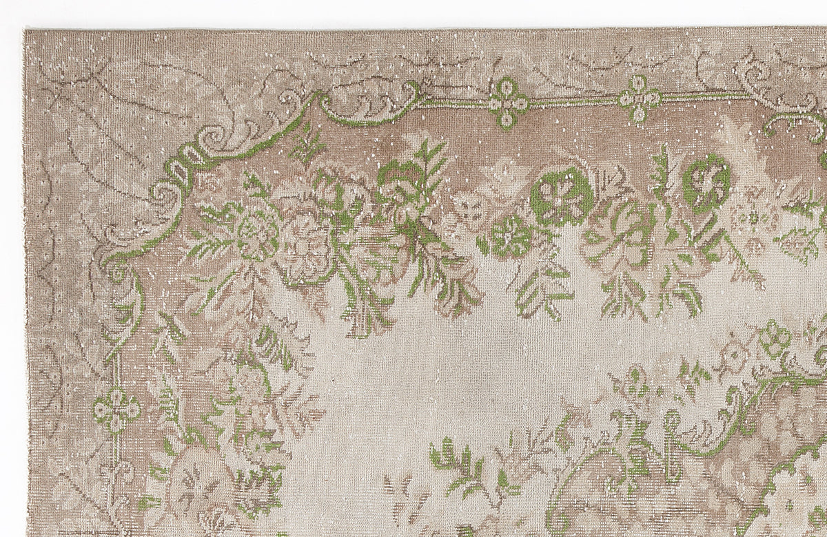 Beige and taupe distressed rug with a faded floral medallion pattern and vibrant green accents.