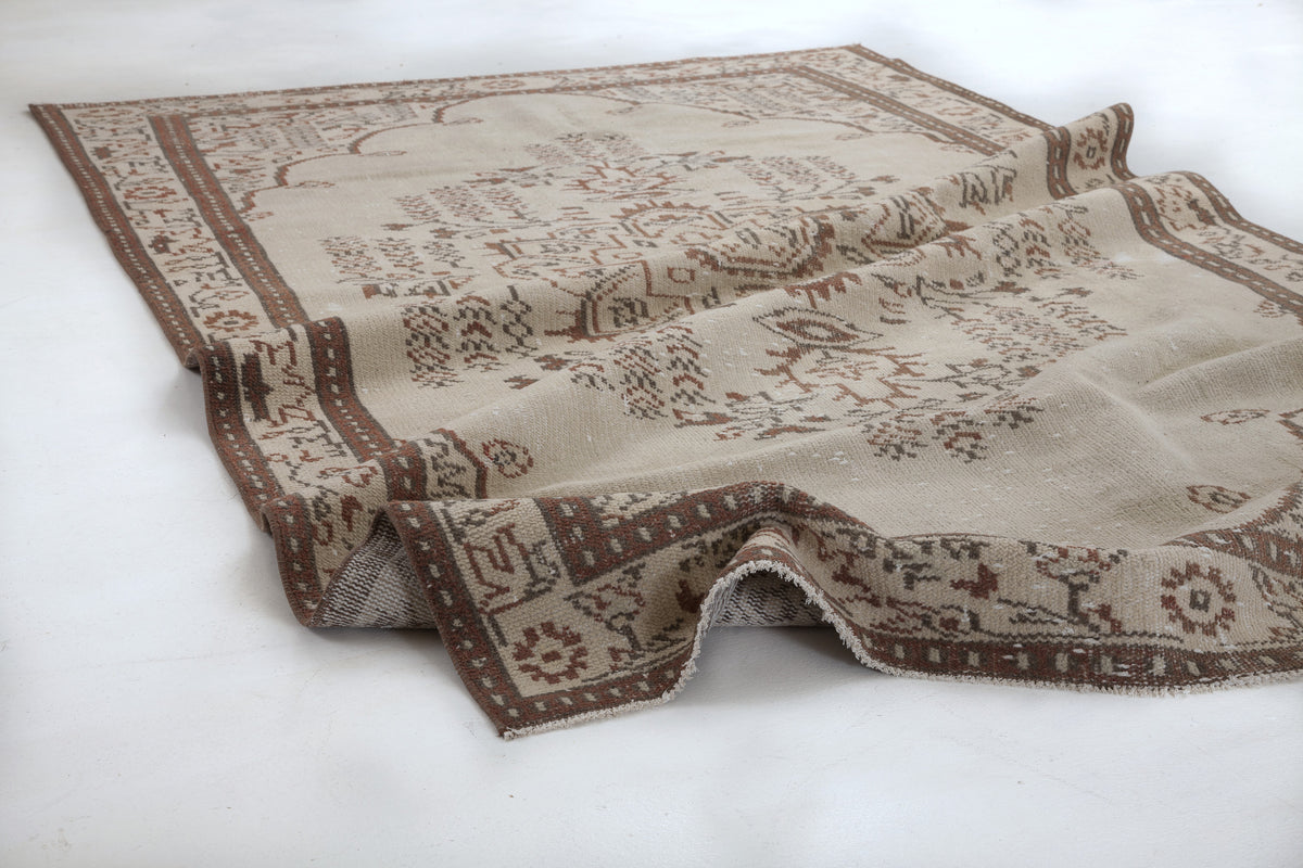 Beige and brown traditional rug with a distressed geometric and floral pattern on a white background.