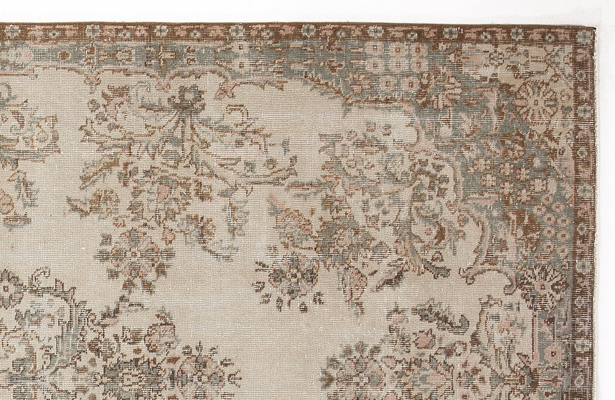 Beige rug with a distressed floral medallion pattern in muted brown, sage green, and soft pink tones.