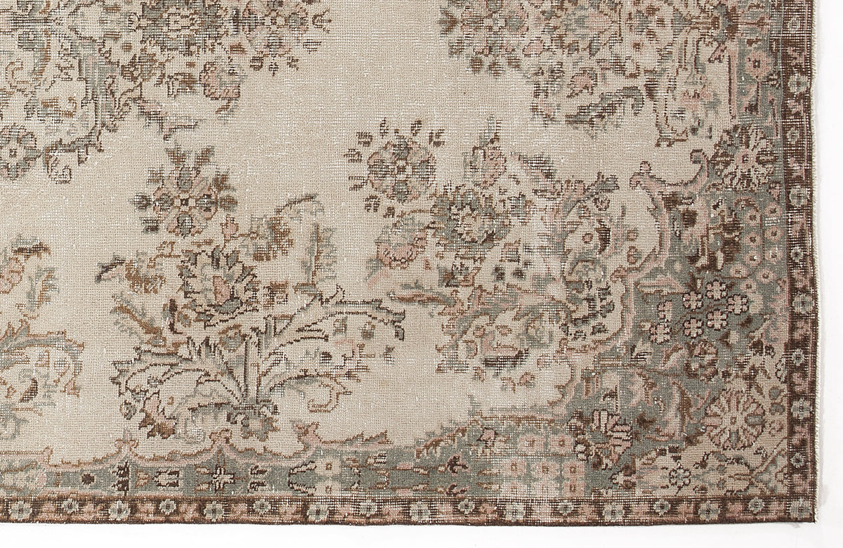 Beige rug with a distressed floral medallion pattern in muted sage green, brown, and soft pink tones.