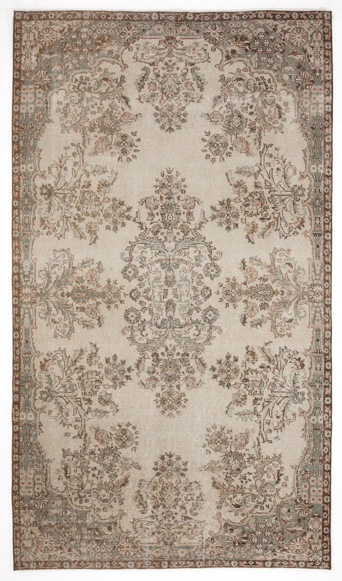 Beige traditional rug with a distressed floral medallion pattern in muted brown, sage green, and soft pink tones.